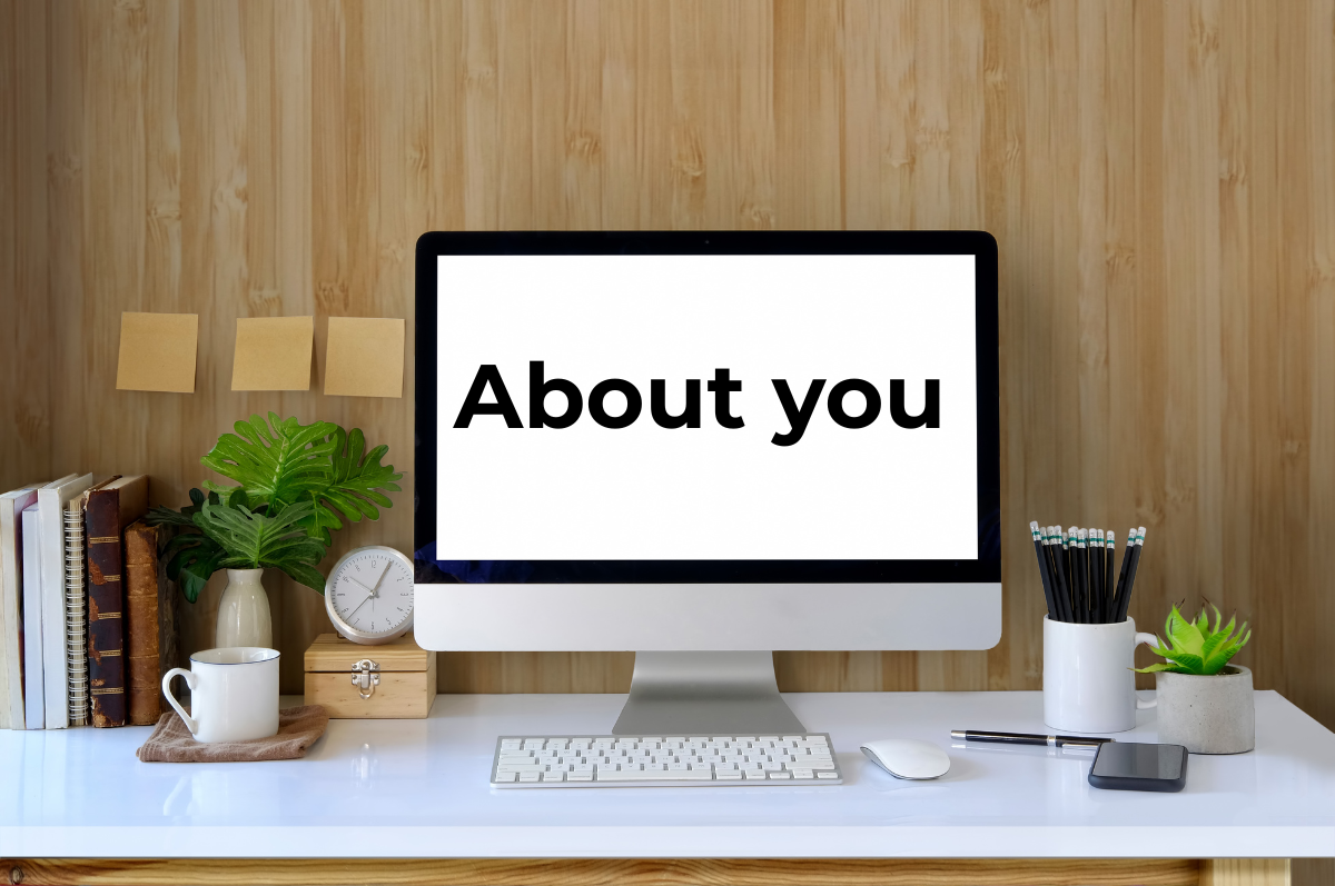 A tidy desk, on it a computer screen featuring the words 'About you'