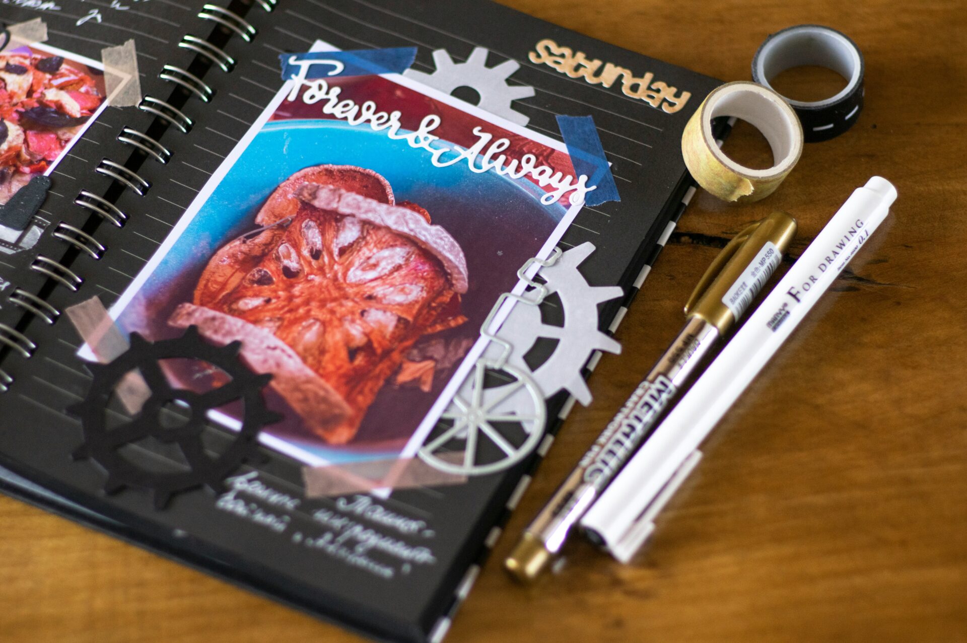 Photo of a journal-style scrapbook, black pages, with colourful things on it, and pens beside it