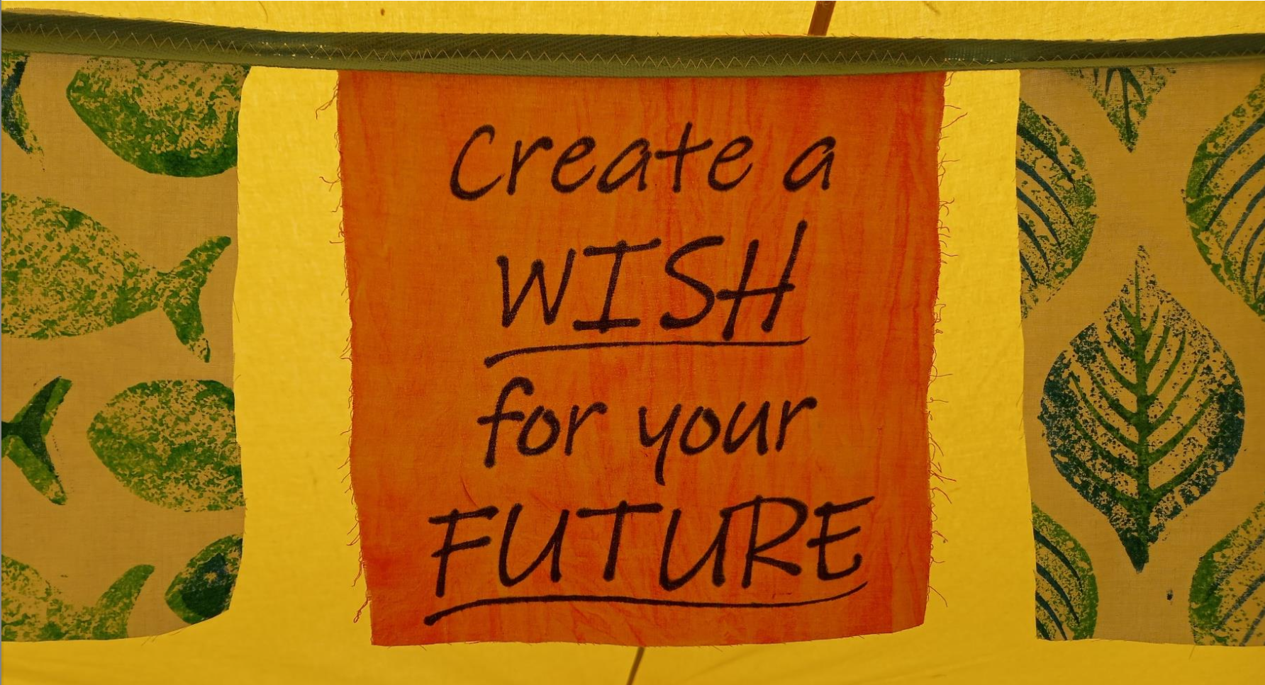 Yellow fabric screen printed with green leaves, and in the centre, the words 'Create a wish for your future'