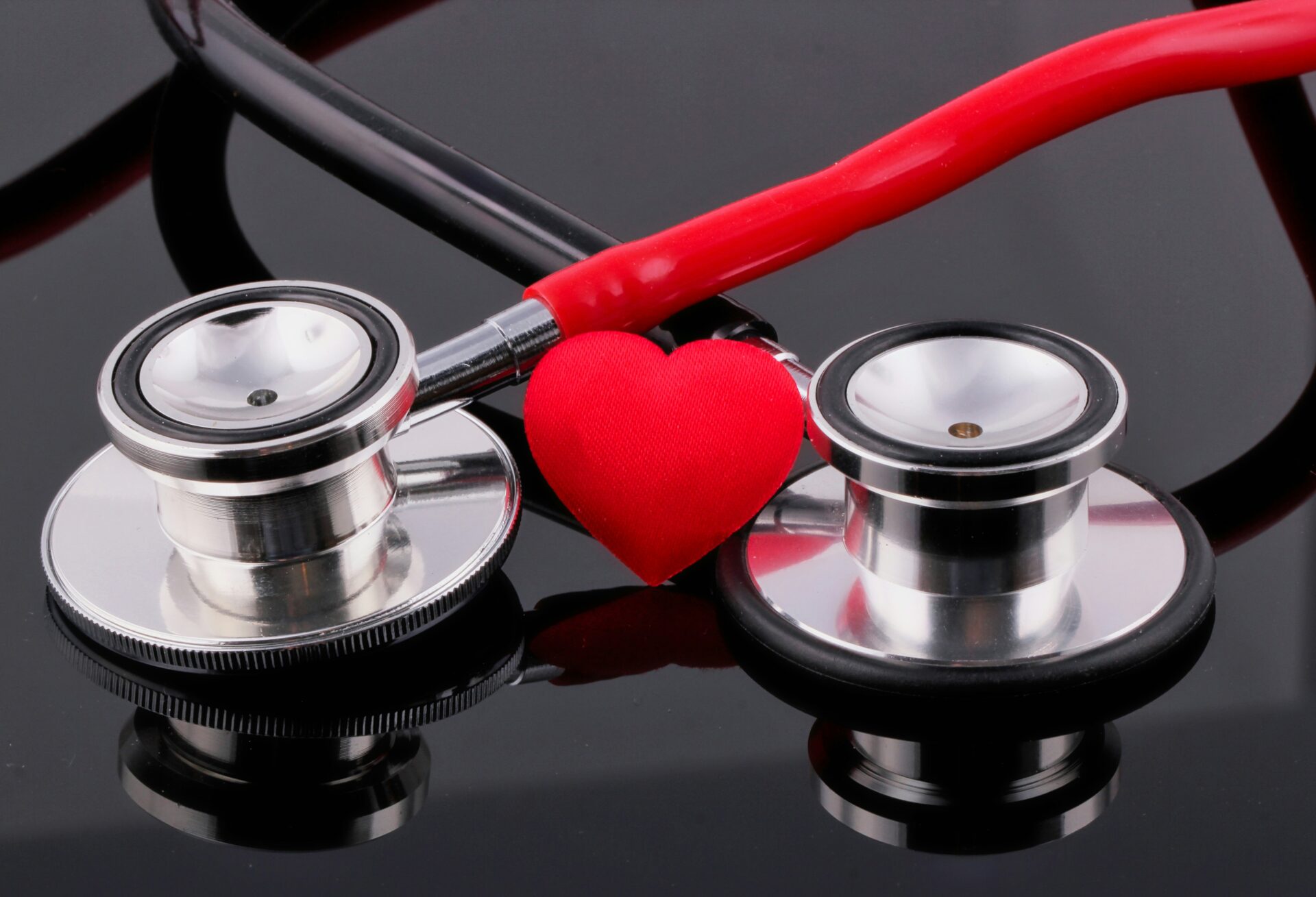 A doctor's stethoscope draped around a red fabric heart on a black table